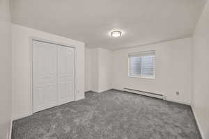 Unfurnished bedroom featuring baseboard heating, a closet, and carpet flooring