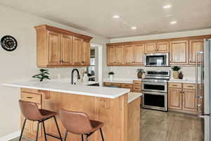 Kitchen featuring a peninsula, stainless steel appliances, a breakfast bar area, light wood finished floors, and recessed lighting
