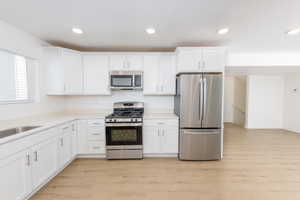 Kitchen featuring stainless steel appliances, white cabinetry, light wood finished floors, recessed lighting, and light stone counters