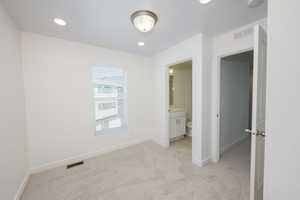 Unfurnished bedroom featuring light carpet, ensuite bathroom, and recessed lighting