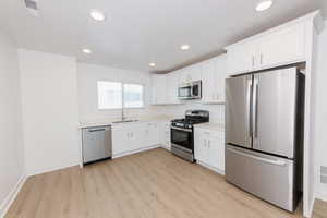 Kitchen featuring stainless steel appliances, white cabinets, light wood-style floors, and recessed lighting