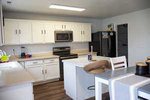 Kitchen with stainless steel appliances, white cabinetry, light countertops, a kitchen bar, and dark wood-type flooring