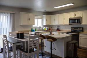 Kitchen featuring light countertops, electric stove, white cabinets, stainless steel microwave, and dark wood-style flooring