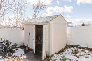 Snow covered structure featuring a storage unit and a fenced backyard