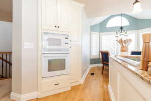 Kitchen featuring white appliances, white cabinets, light wood finished floors, pendant lighting, and light stone counters