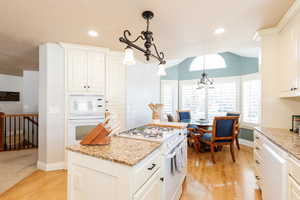 Kitchen featuring white appliances, a kitchen island, light wood-style flooring, white cabinetry, and light stone counters