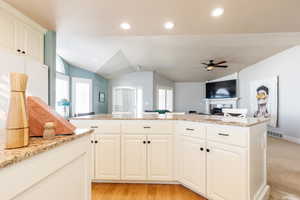 Kitchen featuring light stone countertops, lofted ceiling, white cabinets, open floor plan, and recessed lighting