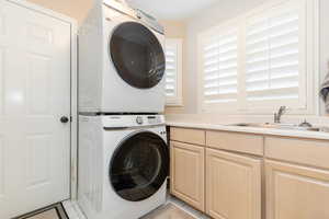 Laundry room featuring stacked washing machine and dryer, light tile patterned floors, and cabinet space