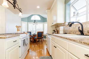 Kitchen featuring white appliances, light stone countertops, light wood-type flooring, vaulted ceiling, and white cabinetry