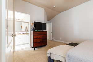 Bedroom with light colored carpet, vaulted ceiling, and connected bathroom