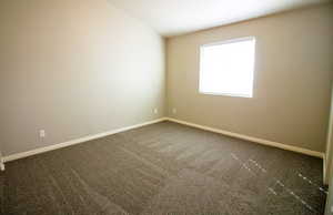 Spare room featuring dark carpet and baseboards