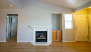 Unfurnished living room featuring light wood-style flooring, a fireplace with raised hearth, and lofted ceiling