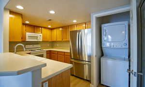 Kitchen featuring recessed lighting, white appliances, light countertops, stacked washing machine and dryer, and a peninsula