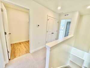 Hall featuring an upstairs landing, light colored carpet, and recessed lighting