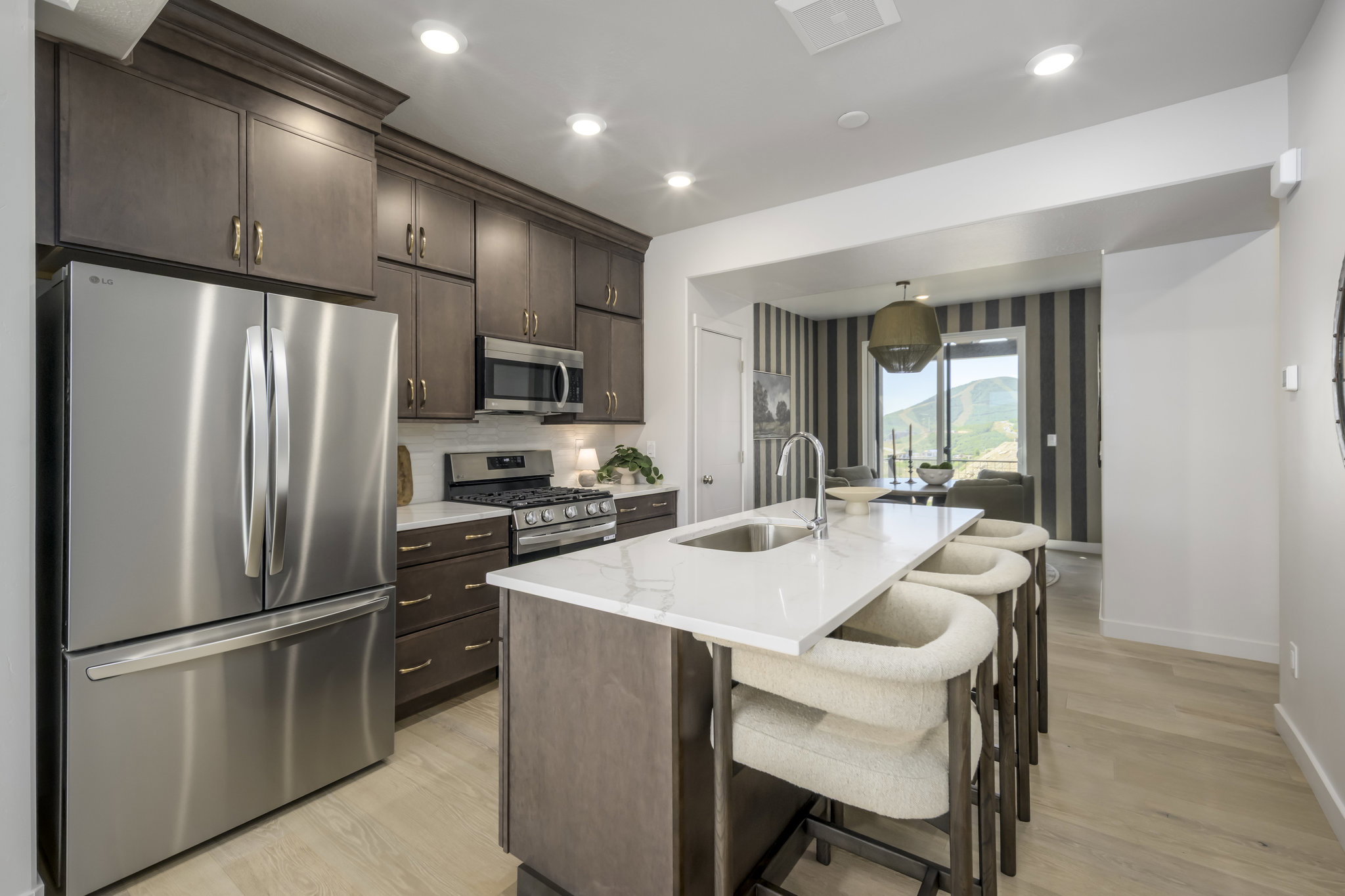 Modern kitchen featuring an island with a stainless steel sink, sleek countertops, extensive dark wood cabinetry, and stainless steel appliances