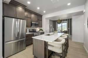 Modern kitchen featuring an island with a stainless steel sink, sleek countertops, extensive dark wood cabinetry, and stainless steel appliances