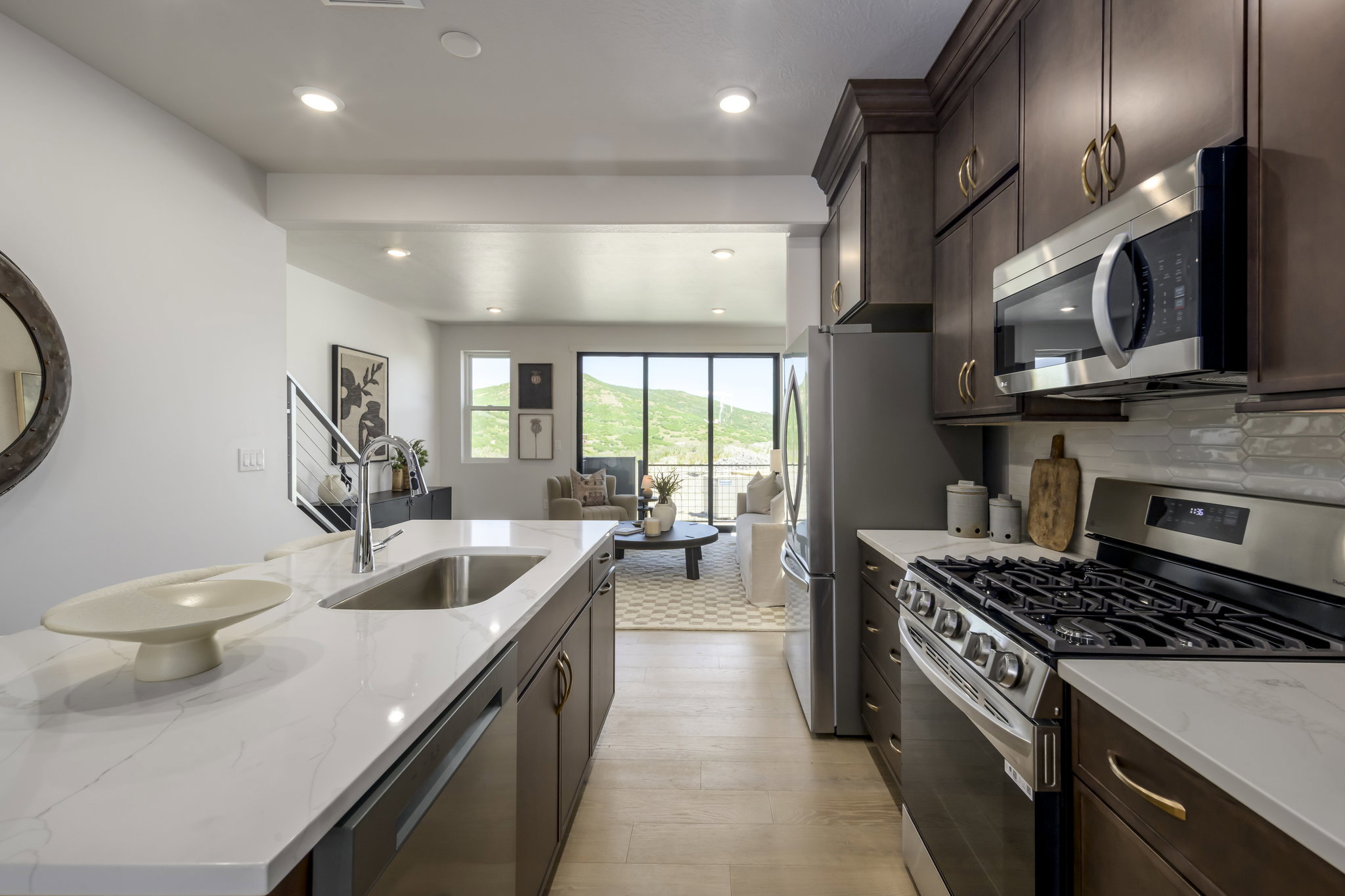 Open-concept kitchen featuring dark wood cabinetry, stainless steel appliances, a gas range, and a spacious island with an undermount sink and light-toned countertop