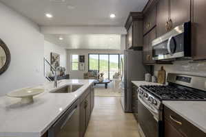 Open-concept kitchen featuring dark wood cabinetry, stainless steel appliances, a gas range, and a spacious island with an undermount sink and light-toned countertop