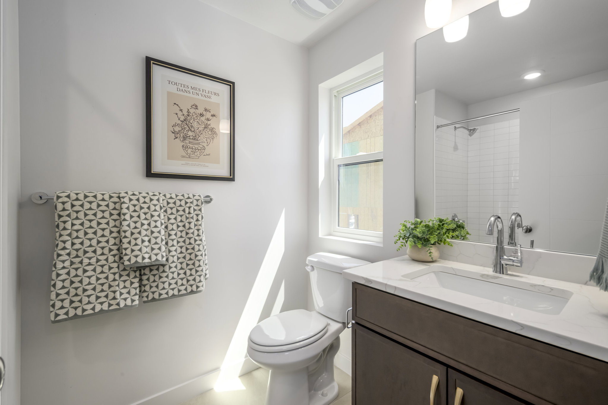 Bathroom featuring a vanity with a white countertop and undermount sink, dark wood-finish cabinetry, chrome fixtures, and a framed mirror