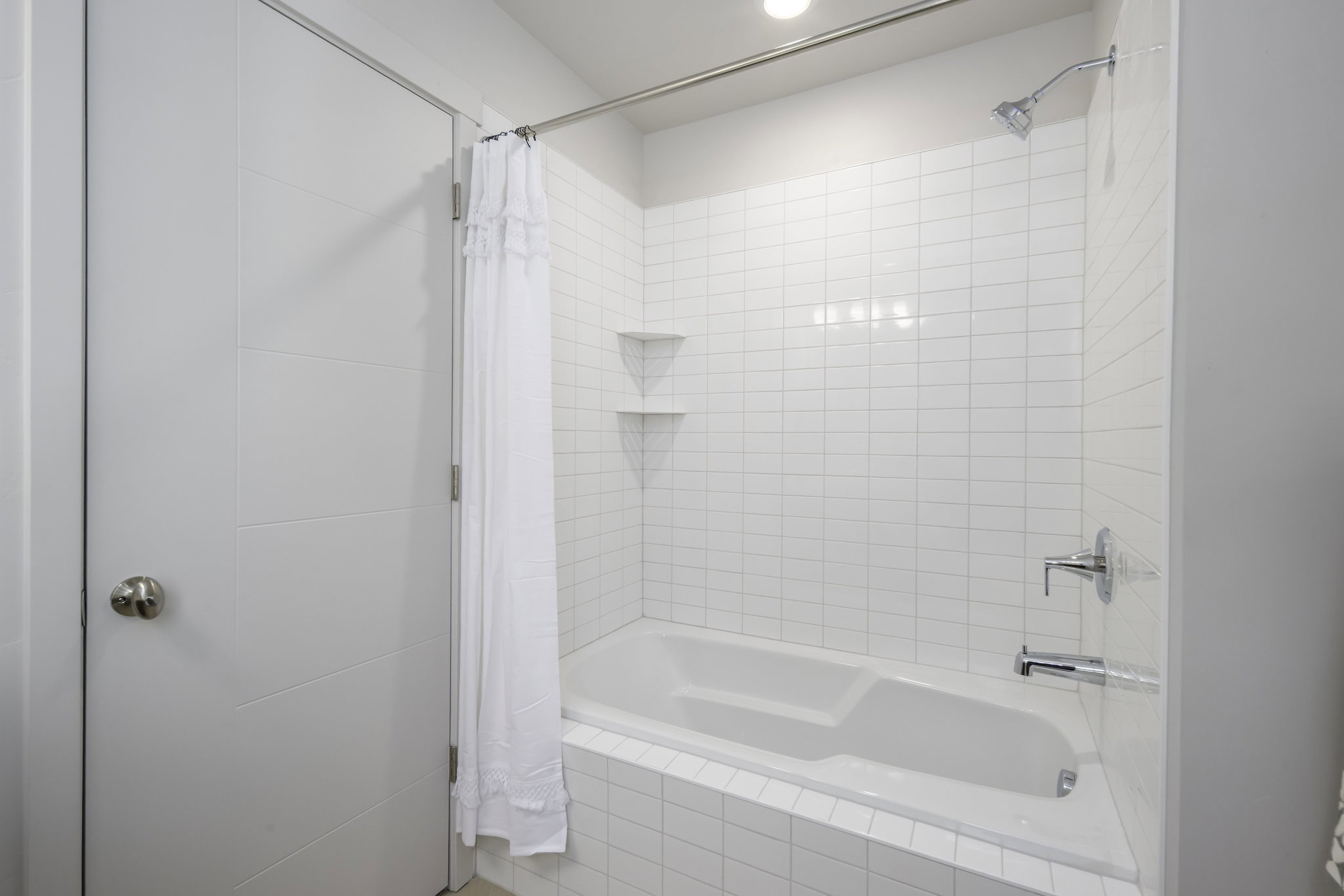 Full bathtub and shower combination featuring white subway tile surround, chrome fixtures, built-in corner shelving, and recessed overhead lighting