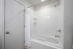 Full bathtub and shower combination featuring white subway tile surround, chrome fixtures, built-in corner shelving, and recessed overhead lighting