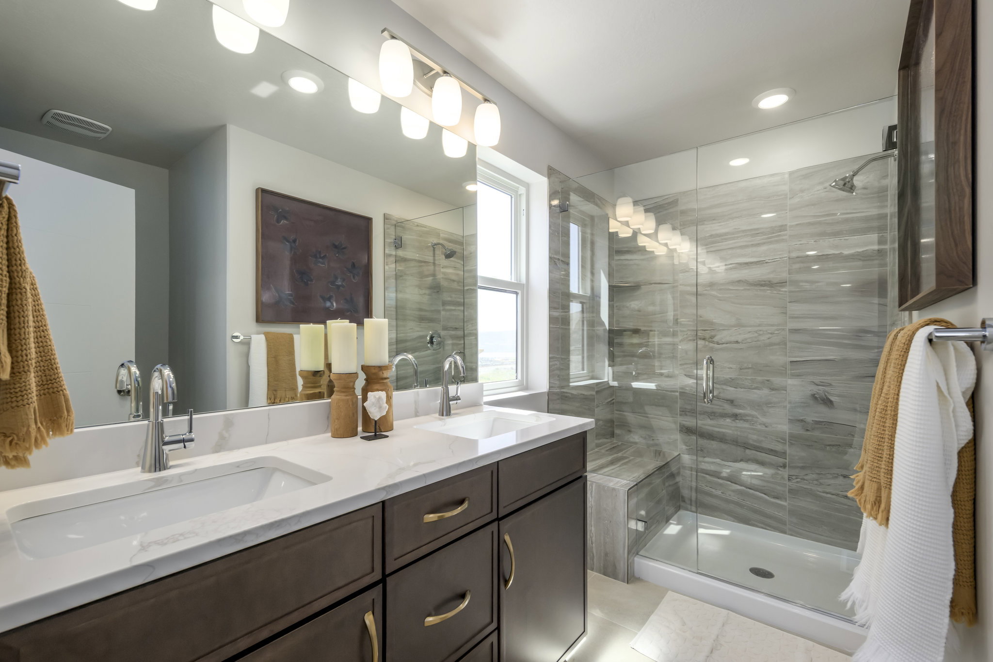 Bathroom featuring a dual vanity with a quartz countertop, dark wood-finish cabinetry, a large frameless mirror, and modern lighting fixtures