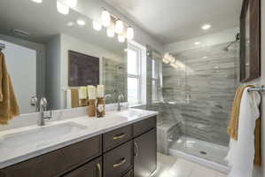 Bathroom featuring a dual vanity with a quartz countertop, dark wood-finish cabinetry, a large frameless mirror, and modern lighting fixtures