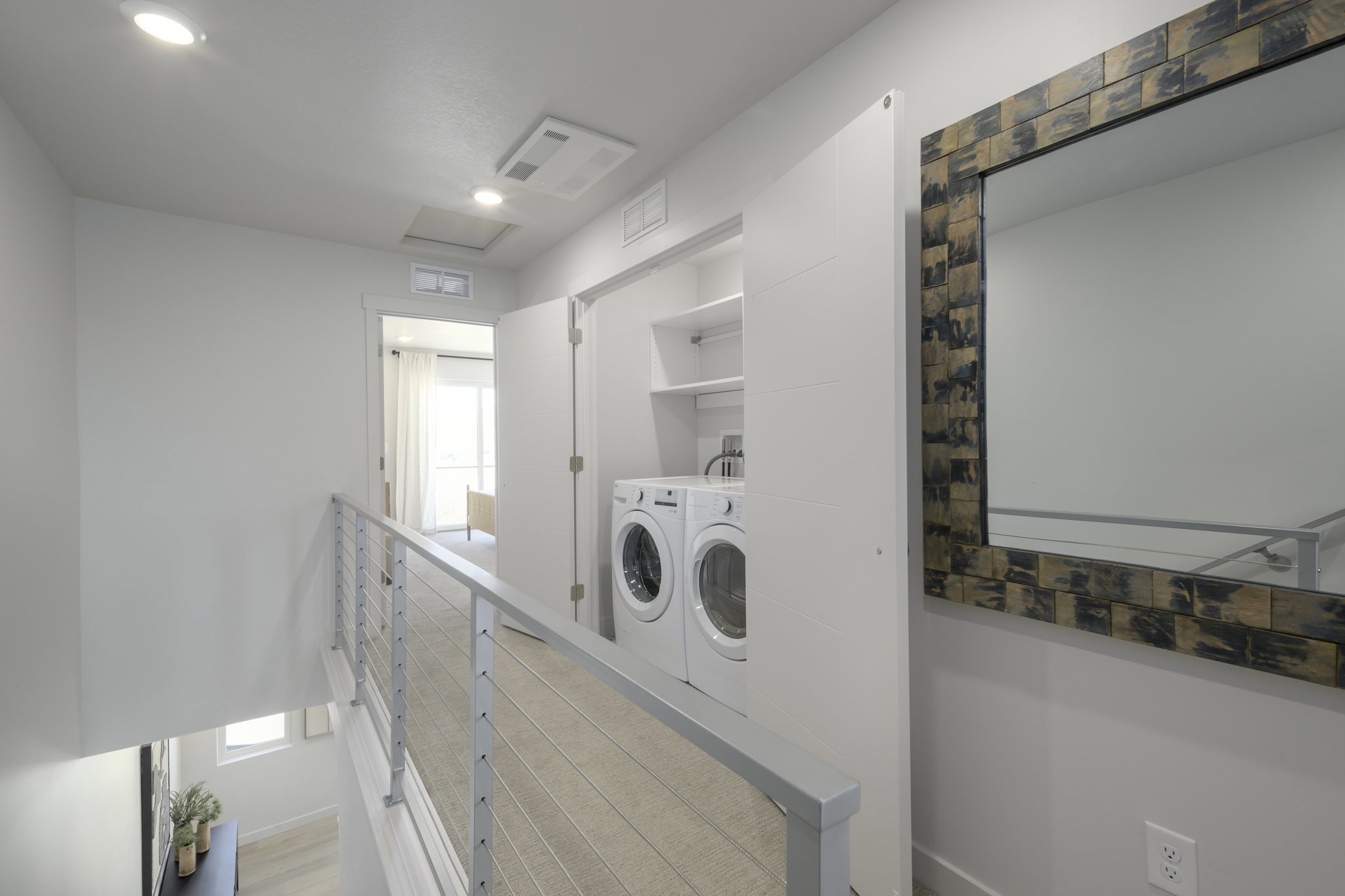 Laundry closet with built-in shelving, front-loading washer and dryer, and modern cable railing
