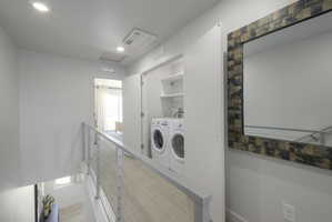 Laundry closet with built-in shelving, front-loading washer and dryer, and modern cable railing