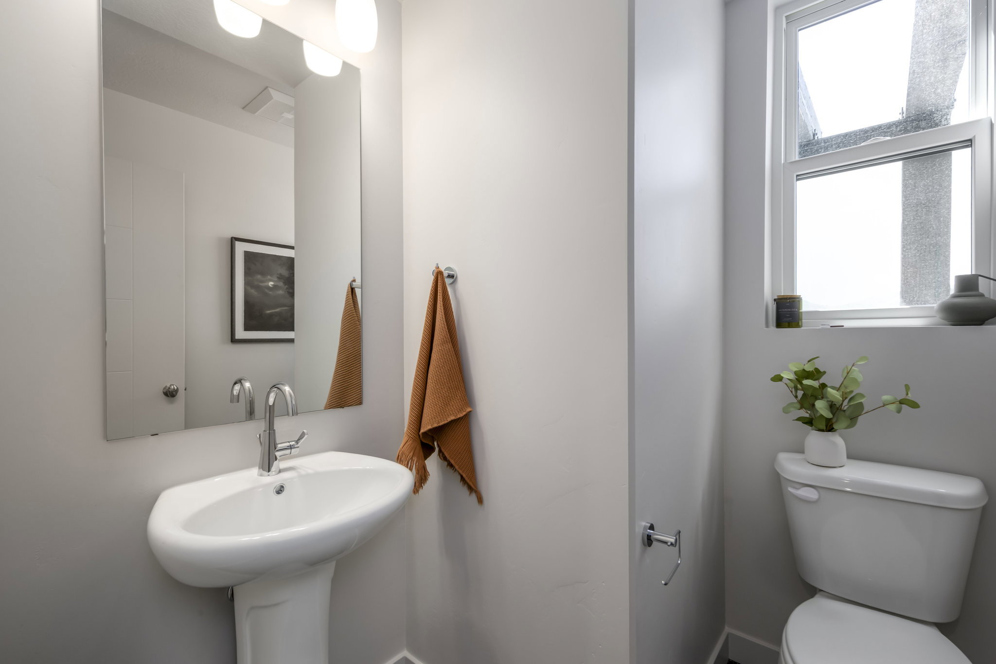 Pedestal sink with chrome faucet, large rectangular mirror, and wall-mounted vanity lighting
