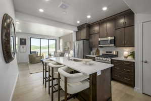 Kitchen featuring dark wood cabinetry, stainless steel appliances, a white subway tile backsplash, and a large island with white countertops