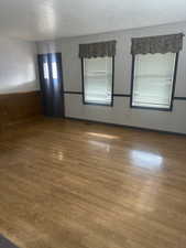 Unfurnished room featuring wood finished floors, a textured ceiling, and wainscoting