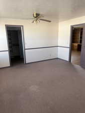 Empty room featuring a textured ceiling, dark colored carpet, and ceiling fan