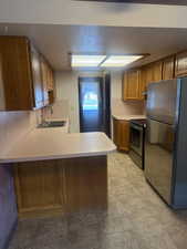 Kitchen featuring wood finish cabinetry, stainless steel appliances, light countertops, and a peninsula