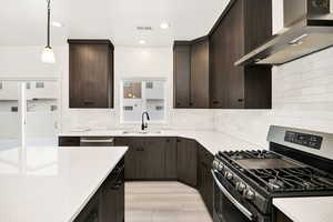 Kitchen with stainless steel appliances, dark wood finish cabinetry, light wood finished floors, light stone counters, and decorative light fixtures
