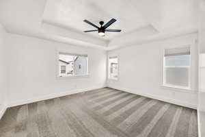 Carpeted spare room with a tray ceiling, a ceiling fan, and a textured ceiling