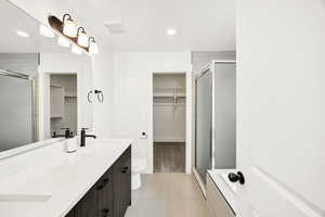 Bathroom with a walk in closet, double vanity, a shower stall, light tile patterned floors, and recessed lighting