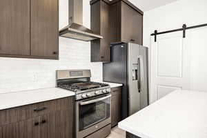Kitchen featuring a barn door, stainless steel appliances, and dark wood finish cabinetry