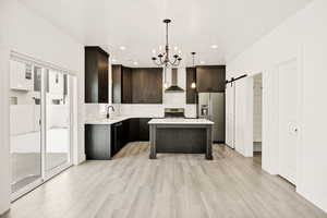 Kitchen featuring a barn door, dark wood finish cabinets, suspended lighting, stainless steel appliances, and a center island