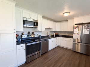 Kitchen with stainless steel appliances, white cabinets, a textured ceiling, dark wood-style floors, and dark stone counters