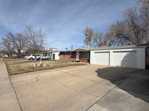 Ranch-style house with a chimney, driveway, a garage, brick siding, and a front yard