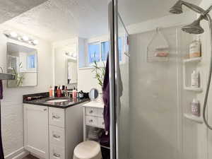 Bathroom with a textured wall, a textured ceiling, vanity, and a stall shower