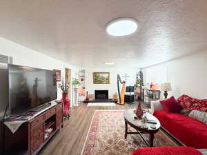 Living area featuring a textured ceiling, a fireplace, and wood finished floors