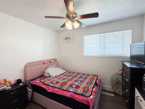 Bedroom with a textured ceiling, ceiling fan, and dark wood-style flooring