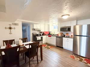 Kitchen featuring stainless steel appliances, white cabinetry, light wood-style flooring, dark countertops, and a textured ceiling