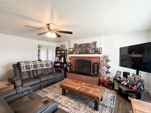 Living area with a textured ceiling, a ceiling fan, wood finished floors, and a brick fireplace