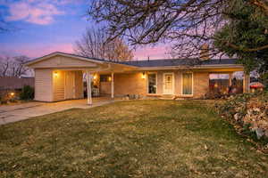 Ranch-style home featuring a front yard, a carport, brick siding, a porch, and driveway