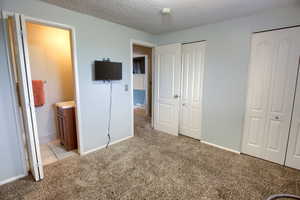 Unfurnished bedroom featuring multiple closets, a textured ceiling, light colored carpet, and ensuite bathroom