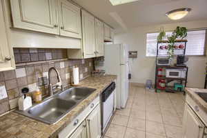 Kitchen featuring tasteful backsplash, white appliances, light tile patterned flooring, and white cabinetry