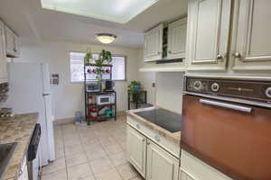 Kitchen featuring white appliances, tile countertops, light tile patterned floors, and white cabinetry